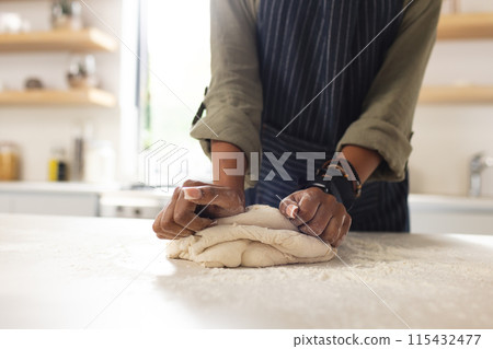 A young African American woman kneads dough on a kitchen counter A young African American woman kneads dough on a kitchen counter 115432477