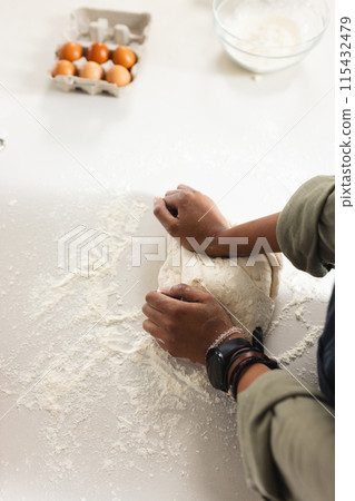 A young African American woman kneads dough on a floured surface with copy space 115432479