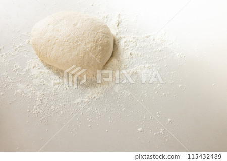 A ball of dough sits atop a dusting of flour on a white surface with copy space 115432489
