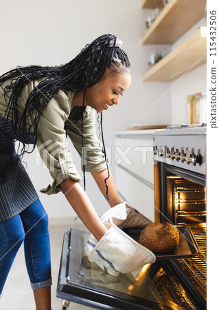 A young African American woman takes a loaf of bread out of an oven 115432506