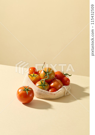Creative photo for advertise product extracted from vegetable ingredient like tomato, a white mesh bag contains red ripe tomatoes placed on light yellow table top. Front view, copy space 115432509