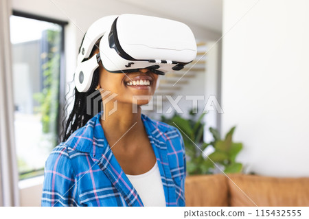 Young African American woman wears a virtual reality headset, smiling in a bright room Young African American woman wears a virtual reality headset, smiling in a bright room 115432555