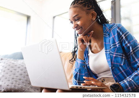 A young African American woman smiles while using a laptop with copy space 115432578