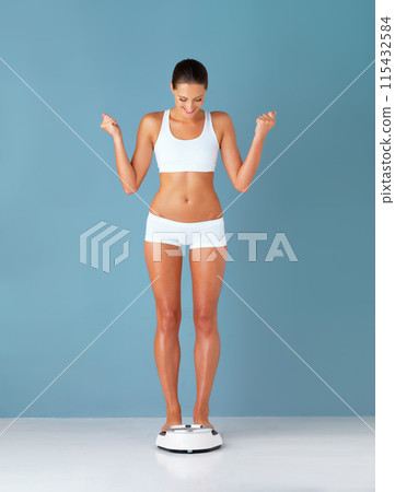 Woman, scale and celebration for weight loss, healthy person and body positivity on blue studio background. Girl, wellness and excited for diet, mockup space and win with victory, success or cheerful 115432584