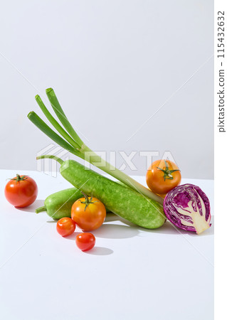 Fresh organic vegetables featured in center of white countertop against light gray background, including green squash, leek, tomato and purple cabbage. Photo for vegan culinary product promotion 115432632