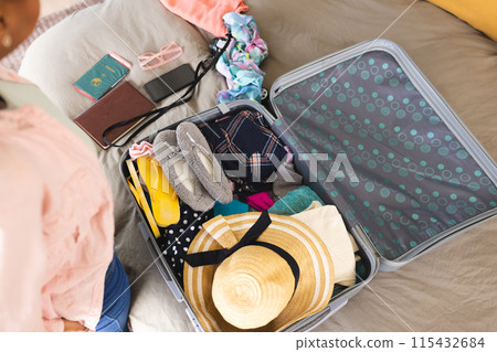 A young African American woman is packing a suitcase with various items 115432684