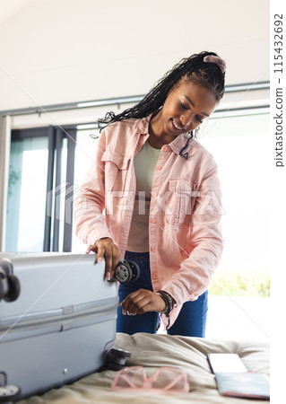A young African American woman packs a suitcase in a bright room 115432692