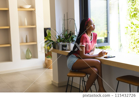 Young African American woman sits at a modern kitchen counter, gazing outside, with copy space Young African American woman sits at a modern kitchen counter, gazing outside, with copy space 115432726