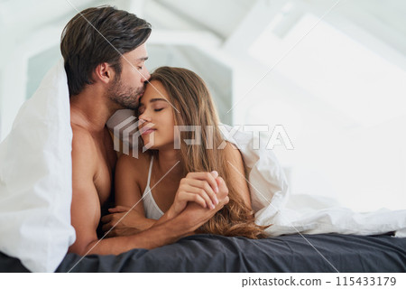 Couple, forehead kiss and embrace in bed for morning romance, love and bonding on weekend. Relationship, man and woman together in home for comfort, relax or care and resting with partner for break 115433179