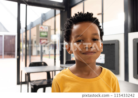 African American boy with a gentle smile, wearing a yellow shirt, in a school classroom 115433242