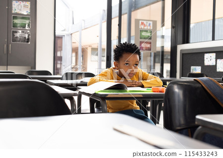 African American boy sits in a school classroom, his expression pensive, with copy space African American boy sits in a school classroom, his expression pensive, with copy space 115433243