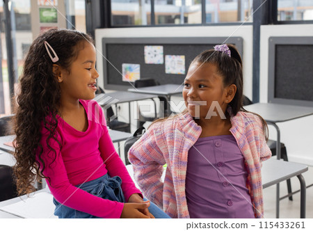 Two biracial girls are sharing a moment in a school classroom setting 115433261