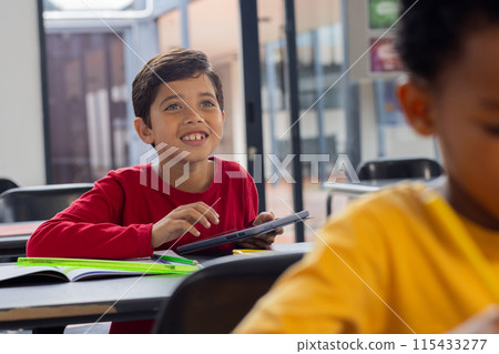 Biracial boy in red smiles with a tablet in a school classroom Biracial boy in red smiles with a tablet in a school classroom 115433277