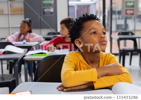 Biracial boy in yellow shirt looks thoughtful in a school classroom setting 115433286