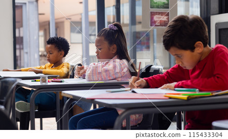 Three children are focused on writing at desks in a school classroom setting 115433304