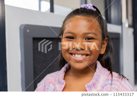 Biracial girl with a bright smile, wearing a purple hair accessory and a knit sweater Biracial girl with a bright smile, wearing a purple hair accessory and a knit sweater 115433317