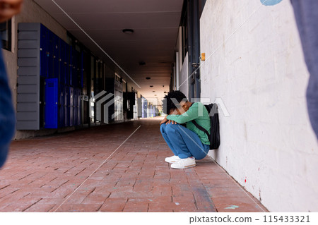 An African American boy sits alone on the ground as a bullying victim in school with copy space An African American boy sits alone on the ground as a bullying victim in school with copy space 115433321
