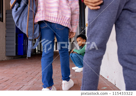 African American boy sits crouched between other children in school, looking sad 115433322