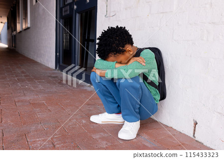 African American boy appears upset, sitting alone with his head down with copy space in school 115433323