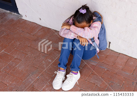 Biracial girl appears upset, sitting on the ground with her head down, with copy space Biracial girl appears upset, sitting on the ground with her head down, with copy space 115433333