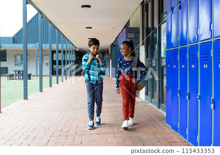 Biracial boy and girl walk through a school corridor, lockers lining the wall Biracial boy and girl walk through a school corridor, lockers lining the wall 115433353