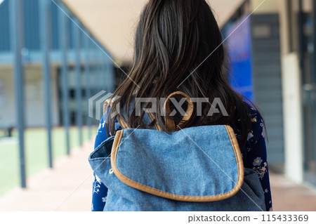 Woman with long dark hair carries a blue denim backpack, standing in a school corridor 115433369