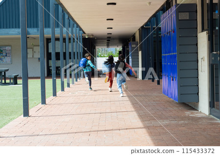 Three children are running through a school corridor with backpacks, with copy space Three children are running through a school corridor with backpacks, with copy space 115433372