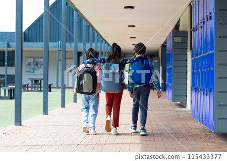 Three children are walking down a school corridor, arms over each other's shoulders 115433377