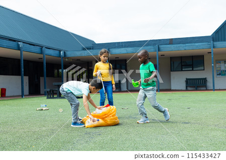 Biracial girl in a yellow top observes as a biracial boy picks up litter 115433427