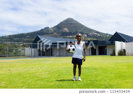 African American boy stands with a soccer ball, smiling on a sunny field with copy space in school African American boy stands with a soccer ball, smiling on a sunny field with copy space in school 115433434