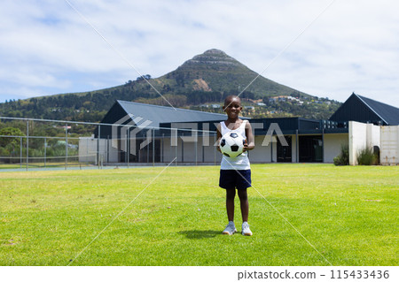 African American boy stands on a grassy field in school holding a soccer ball with copy space African American boy stands on a grassy field in school holding a soccer ball with copy space 115433436
