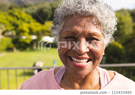 Senior biracial woman with curly gray hair smiles warmly outdoors 115433495