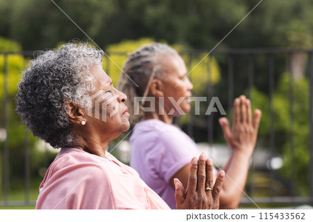 Senior African American woman and senior biracial woman practice yoga outdoors, both with grey hair 115433562