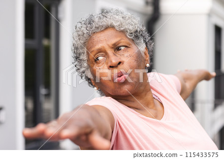 Senior biracial woman with gray hair is stretching her arms outdoors 115433575