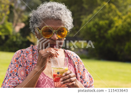 Senior biracial woman with curly gray hair sips a drink through a straw Senior biracial woman with curly gray hair sips a drink through a straw 115433643