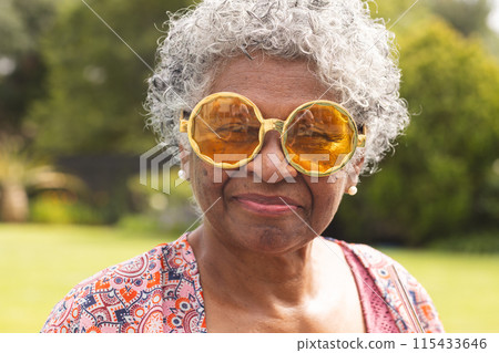Senior biracial woman with gray hair wears large amber sunglasses and pearl earrings Senior biracial woman with gray hair wears large amber sunglasses and pearl earrings 115433646