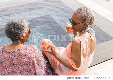 Senior African American woman and senior biracial woman enjoy a poolside chat with copy space Senior African American woman and senior biracial woman enjoy a poolside chat with copy space 115433696