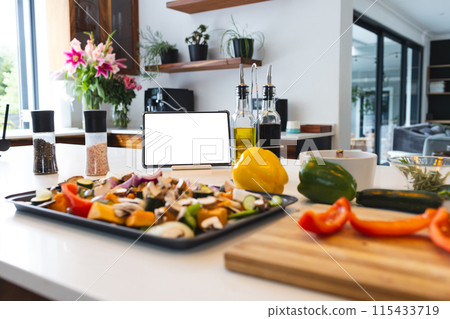 A tablet with a blank screen stands among various cooking ingredients on a kitchen counter 115433719