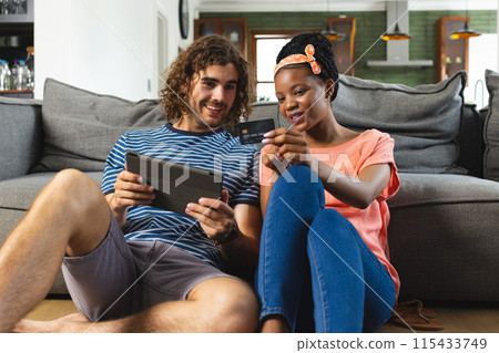 Diverse couple enjoys a digital tablet and a credit card in a cozy living room 115433749