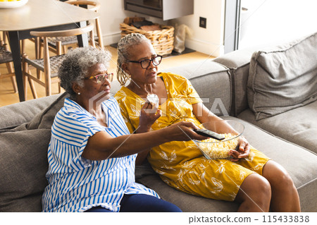 Senior African American woman and senior biracial woman enjoy a movie together, sharing popcorn 115433838