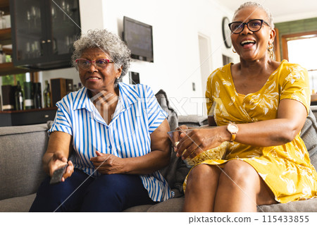 Senior African American woman and senior biracial woman sit together on a couch at home Senior African American woman and senior biracial woman sit together on a couch at home 115433855