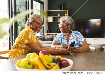 Senior African American woman and senior biracial woman share a moment at a table at home Senior African American woman and senior biracial woman share a moment at a table at home 115433870