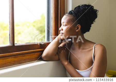A young African American woman gazes out a window, lost in thought, with copy space A young African American woman gazes out a window, lost in thought, with copy space 115433916