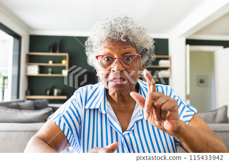 Senior biracial woman with gray hair and glasses gestures with her finger on a video call 115433942