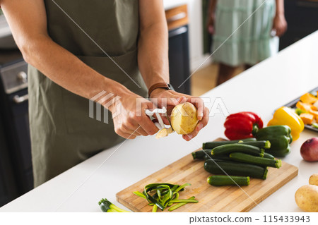 Young Caucasian man peels a potato in a modern kitchen 115433943