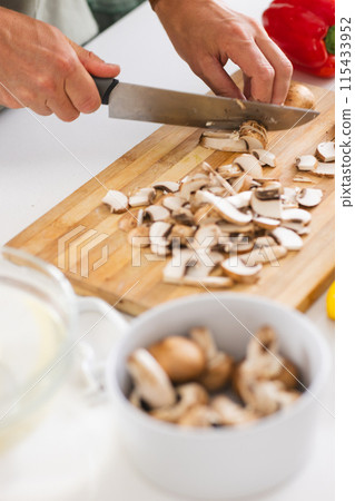 Hands are slicing mushrooms on a wooden cutting board with a kitchen knife Hands are slicing mushrooms on a wooden cutting board with a kitchen knife 115433952