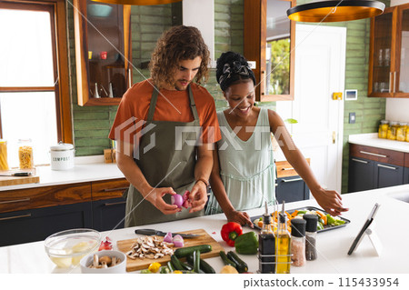 Diverse couple, young African American woman and Caucasian man cook together in a sunny kitchen 115433954