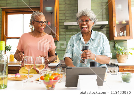 Senior African American woman and senior biracial woman share a joyful moment in a kitchen 115433980