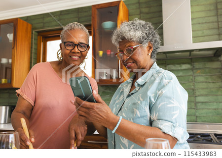 Senior African American woman and senior biracial woman share a moment in a kitchen Senior African American woman and senior biracial woman share a moment in a kitchen 115433983