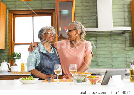 Senior African American woman and senior biracial woman share a warm moment in a sunny kitchen Senior African American woman and senior biracial woman share a warm moment in a sunny kitchen 115434035